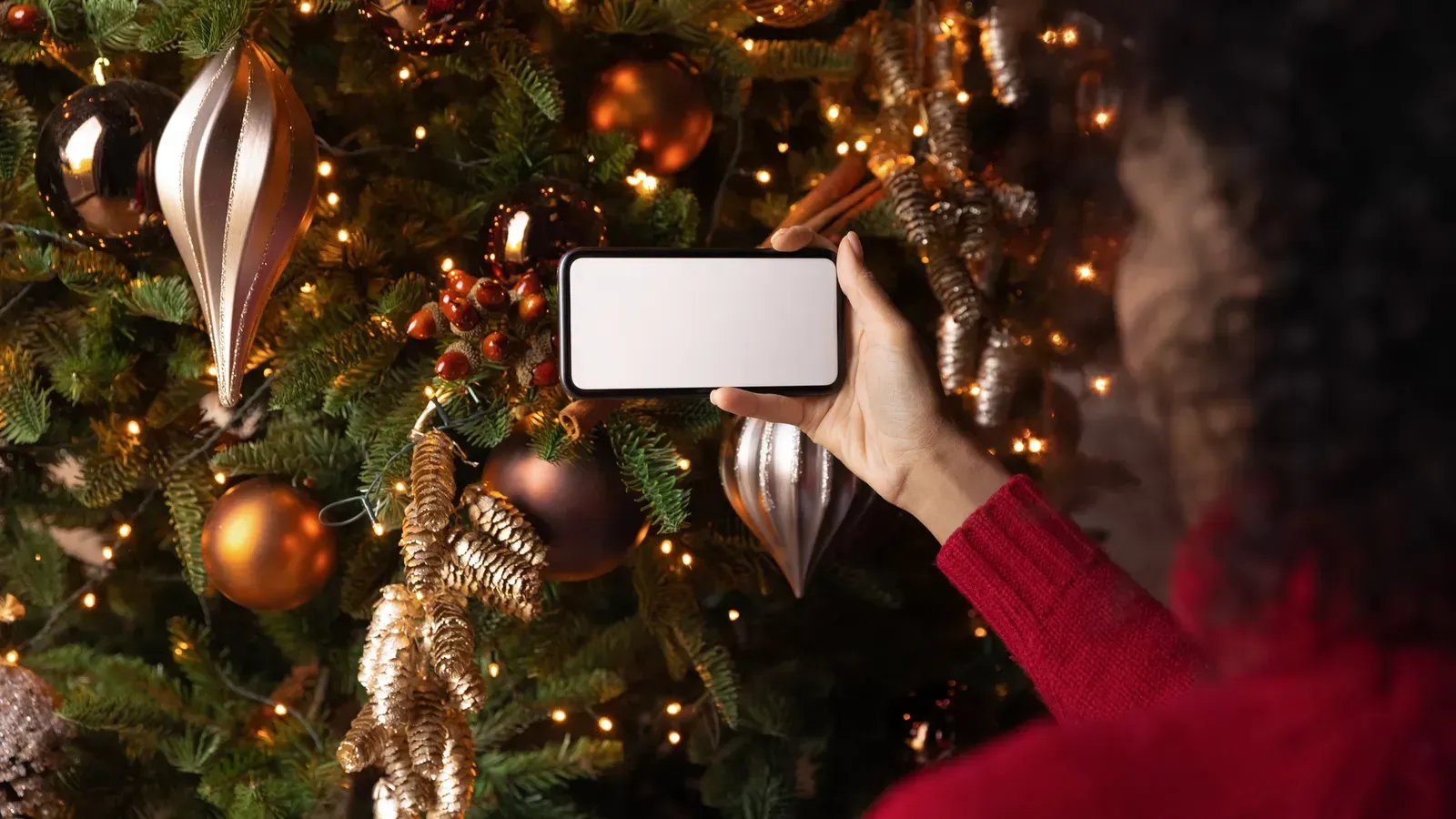 A woman is taking a picture of a christmas tree with her cell phone.