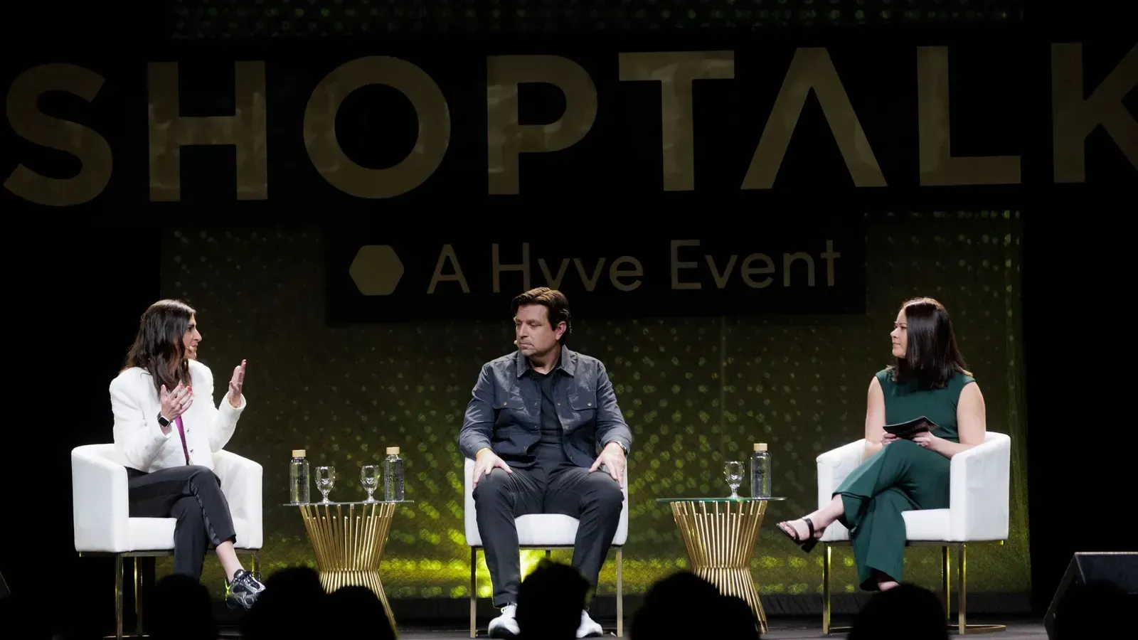 Three people are sitting on a stage at a shoptalk event
