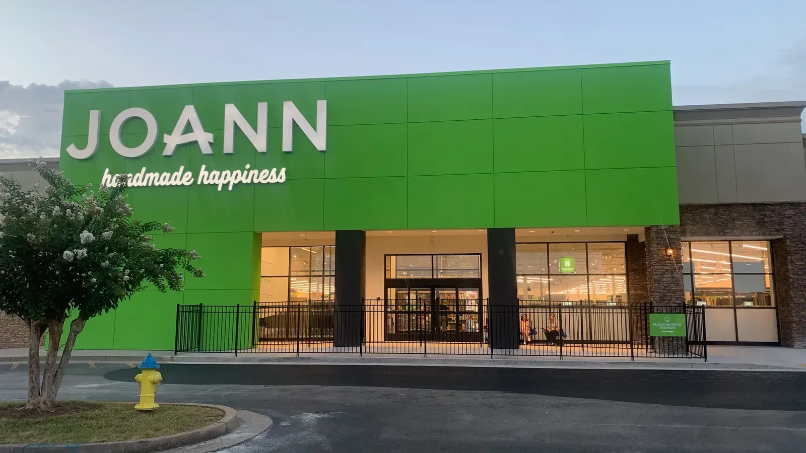 A green joann store with a fire hydrant in front of it.