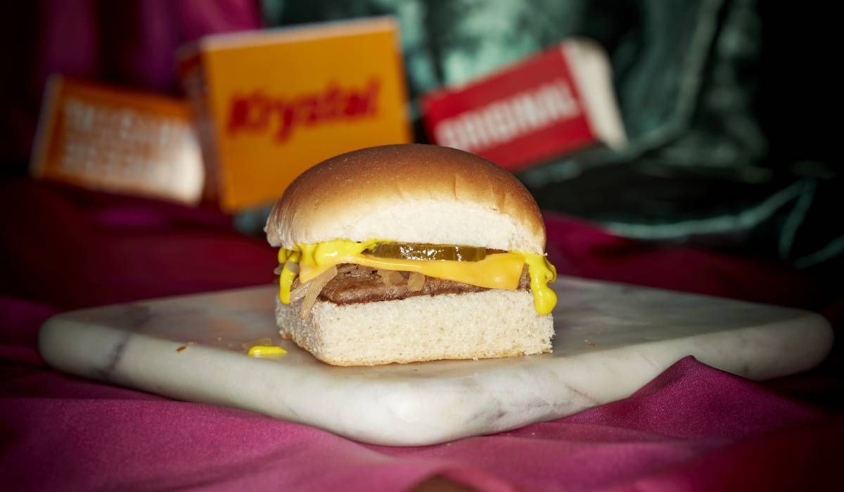 A hamburger on a bun with cheese and mustard on a marble cutting board.