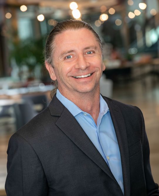 A man in a suit and blue shirt is smiling for the camera.