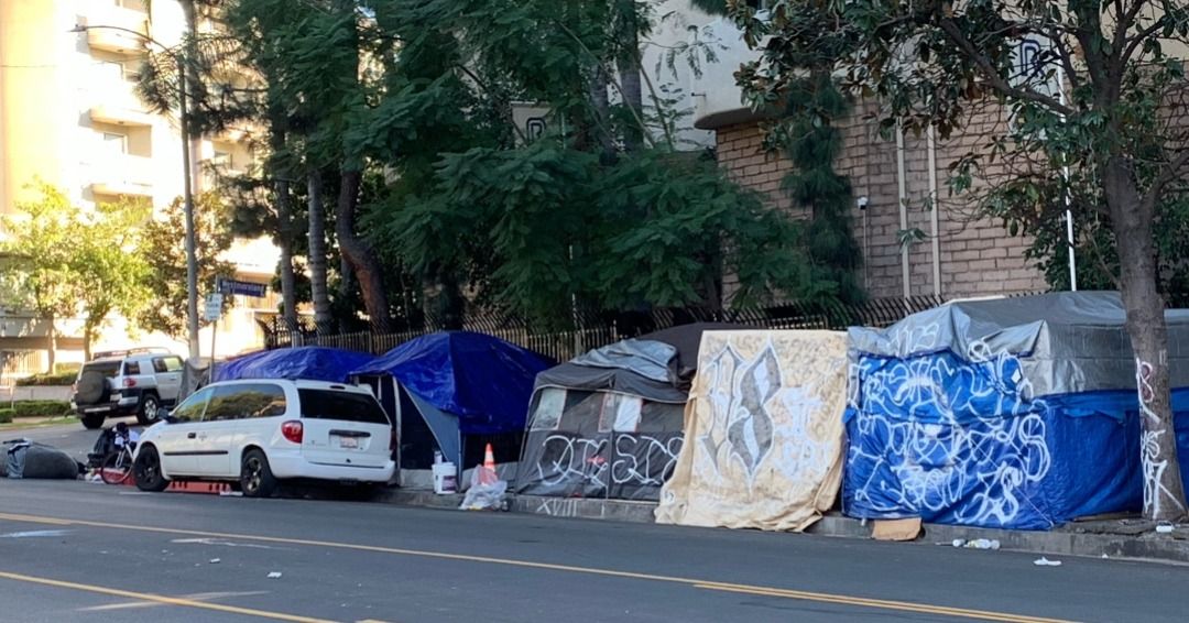 A group of tents are sitting on the side of the road next to a car.
