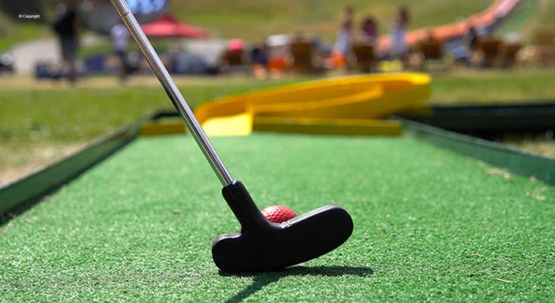 A close up of a golf club and ball on a mini golf course.