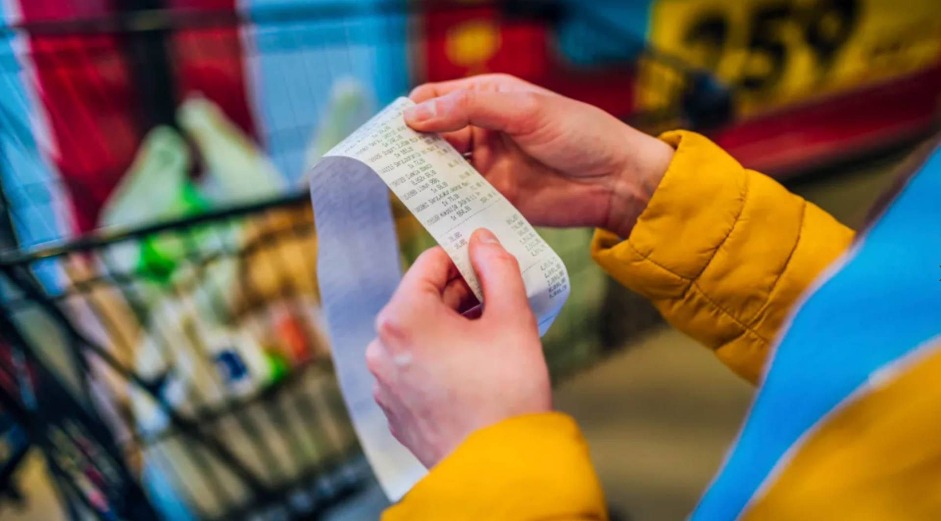 A person is holding a receipt in their hands in front of a shopping cart.