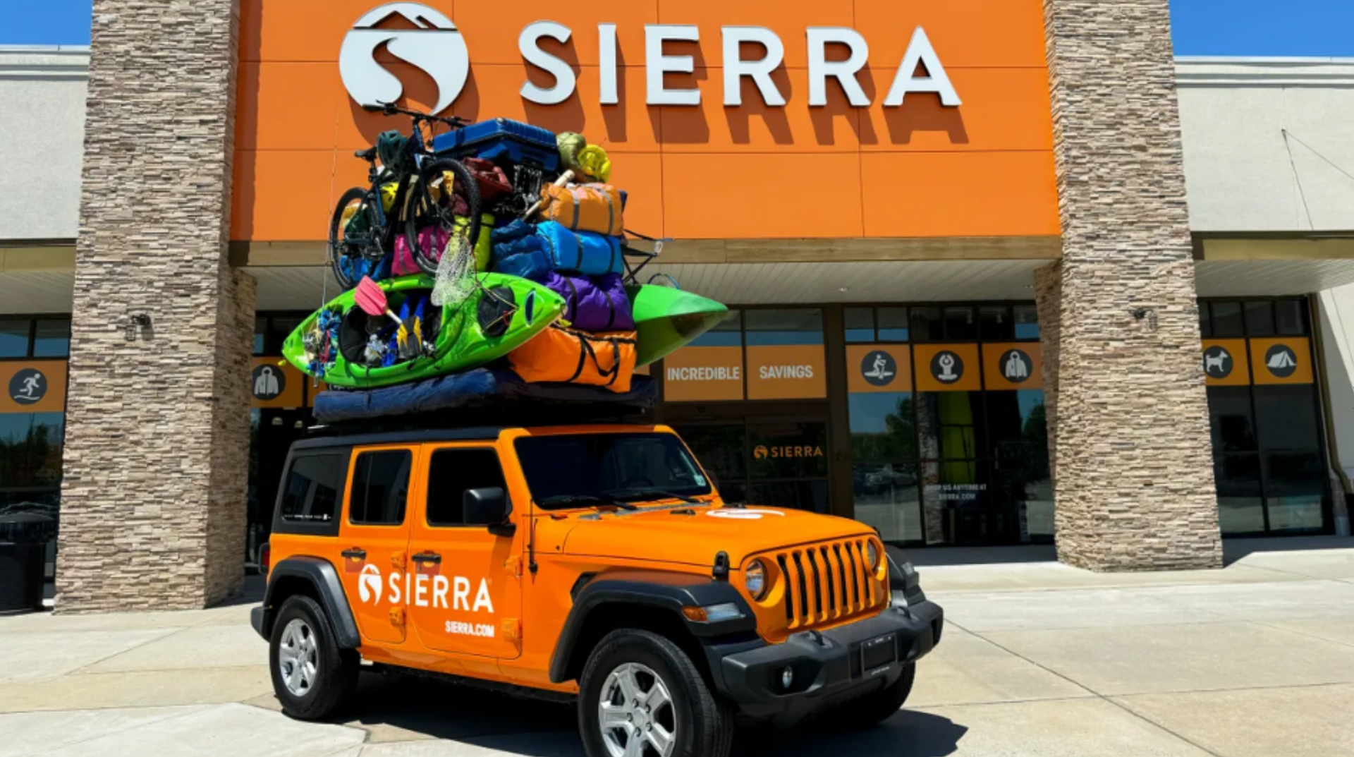 A jeep with kayaks on top of it is parked in front of a sierra store.