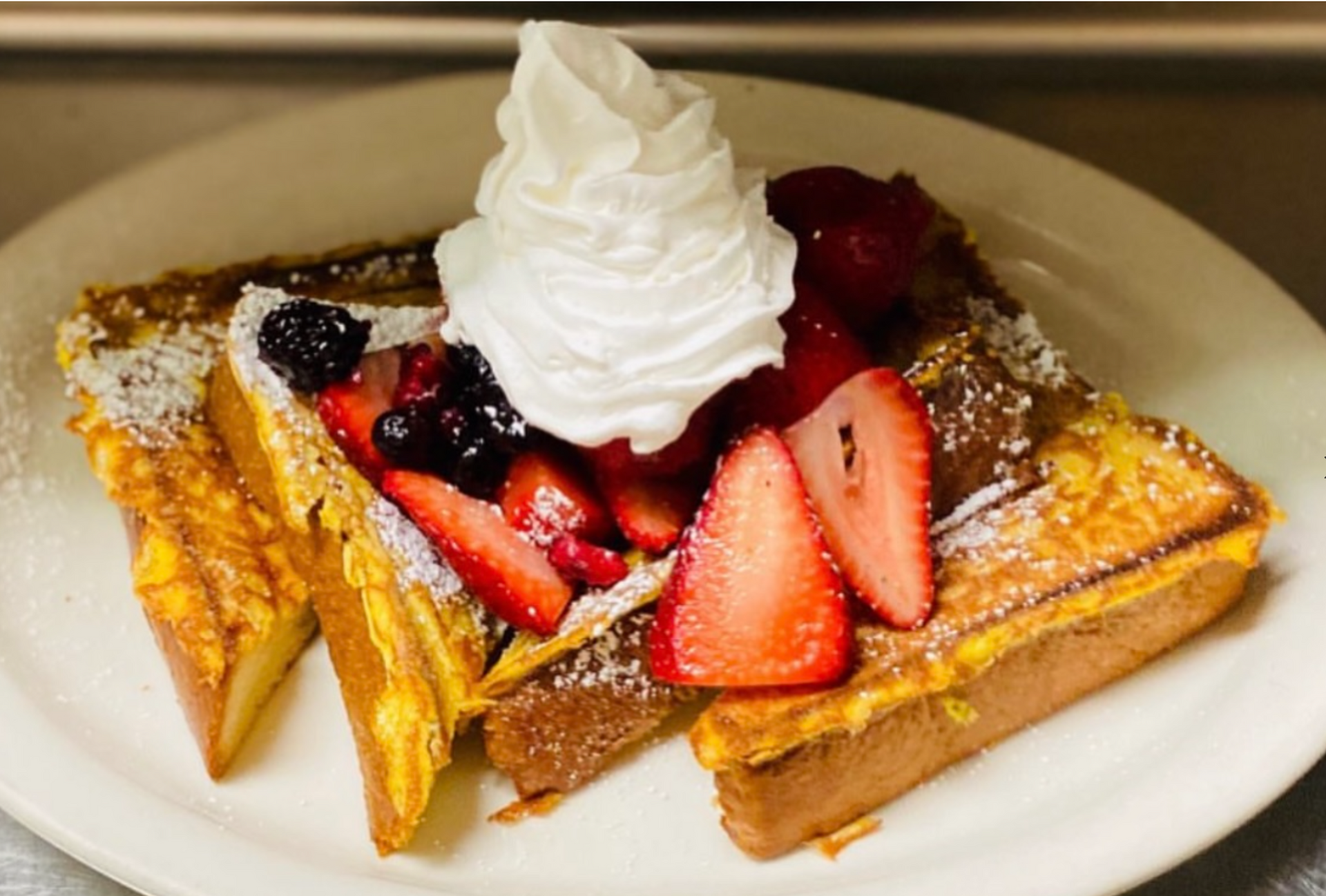 French toast with whipped cream and strawberries on a white plate.