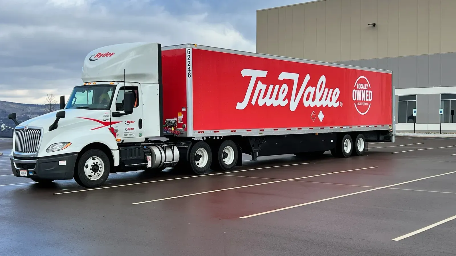 A red and white truck with the word true value on the side is parked in a parking lot.