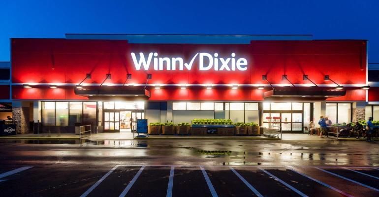 A winn dixie store is lit up at night with a parking lot in front of it.