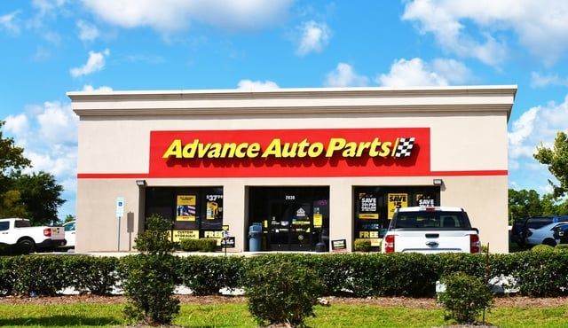 A white truck is parked in front of an advance auto parts store