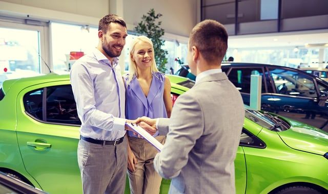 A man and woman are shaking hands with a car dealer in a car showroom.