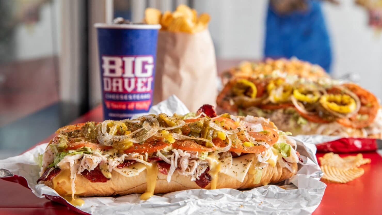 A green Publix Food & Pharmacy sign mounted on a white and beige building exterior against a blue sky.