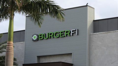 The front of a burger fi restaurant with a palm tree in the foreground.