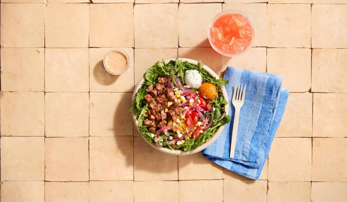 A bowl of salad with a fork and a drink on a table.