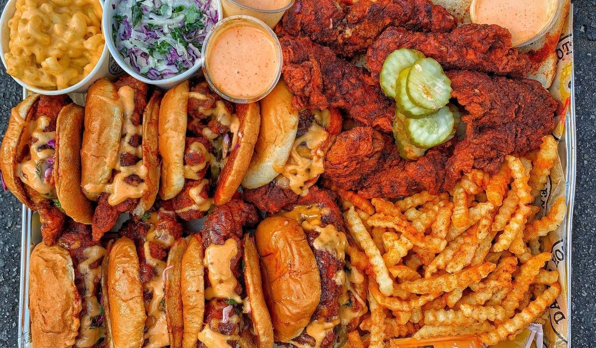 A large tray of food including chicken , french fries , hot dogs , macaroni and cheese and pickles.