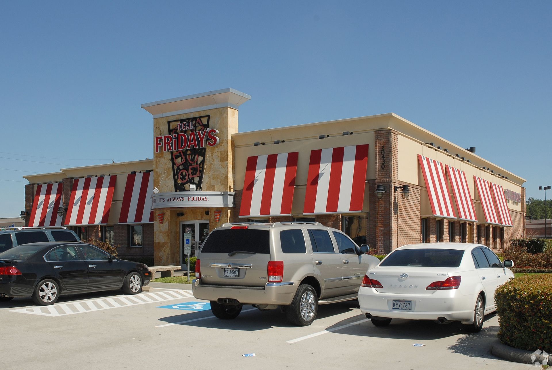 Cars are parked in front of a restaurant with red and white awnings