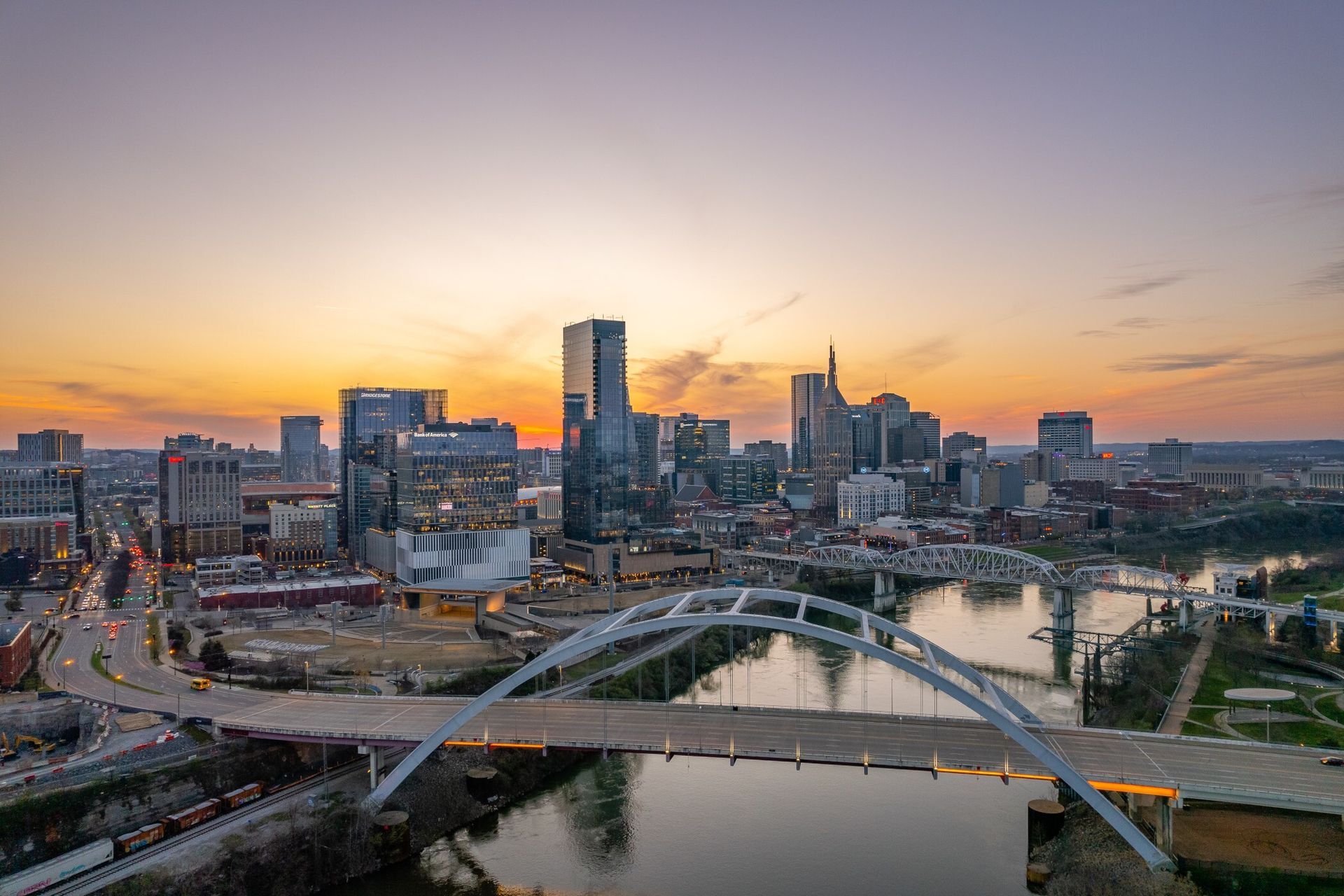 An aerial view of a city skyline with a bridge over a river at sunset.
