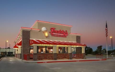 A freddy 's ice cream parlor is located in a parking lot at dusk.