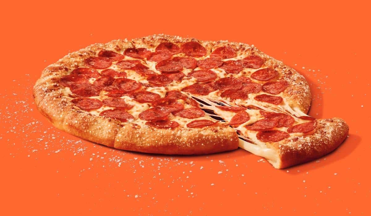 A pepperoni pizza with a slice taken out of it on an orange background.