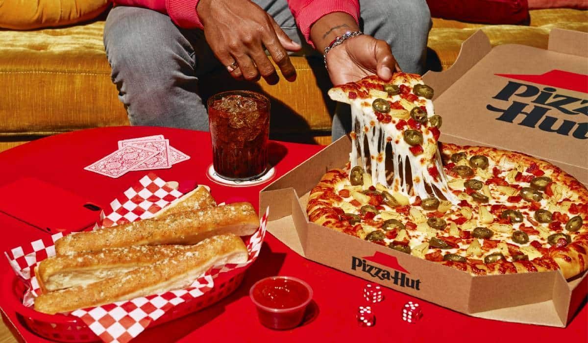 A person is taking a slice of pizza out of a pizza hut box.