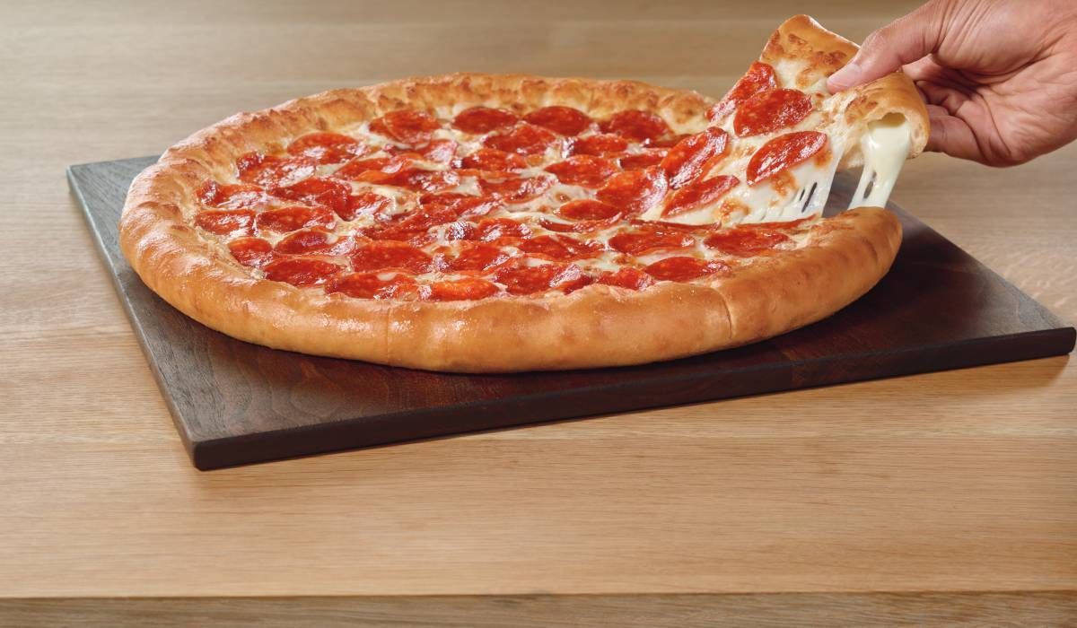 A person is taking a slice of pepperoni pizza from a pizza on a wooden cutting board.