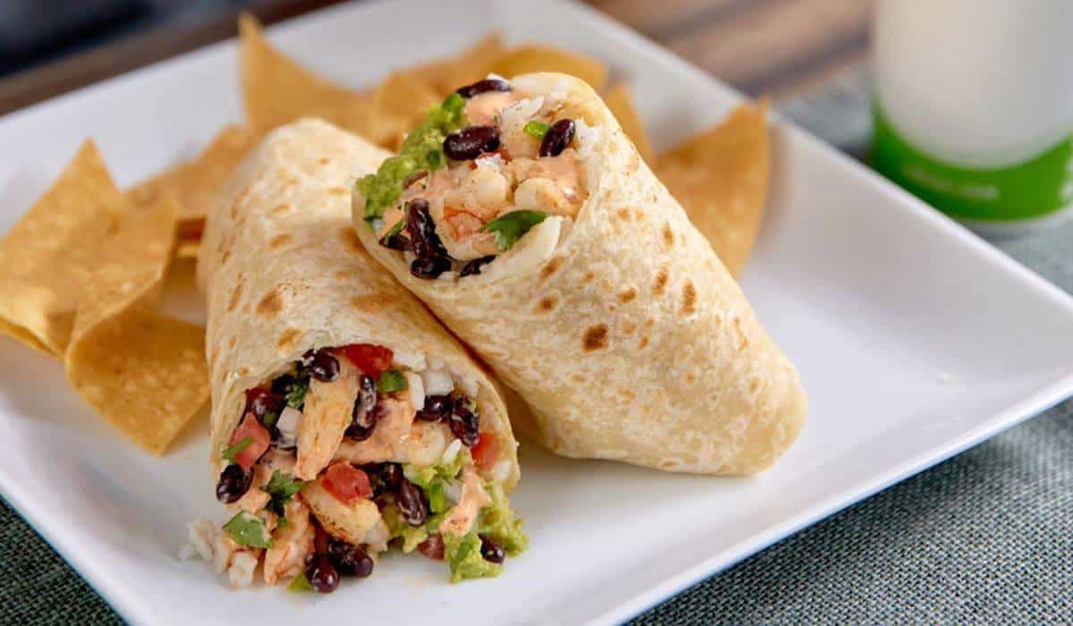Two burritos are on a white plate with tortilla chips.