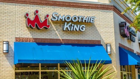 The front of a smoothie king restaurant with a blue awning.