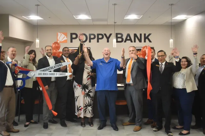 A group of people are standing in front of a poppy bank sign.