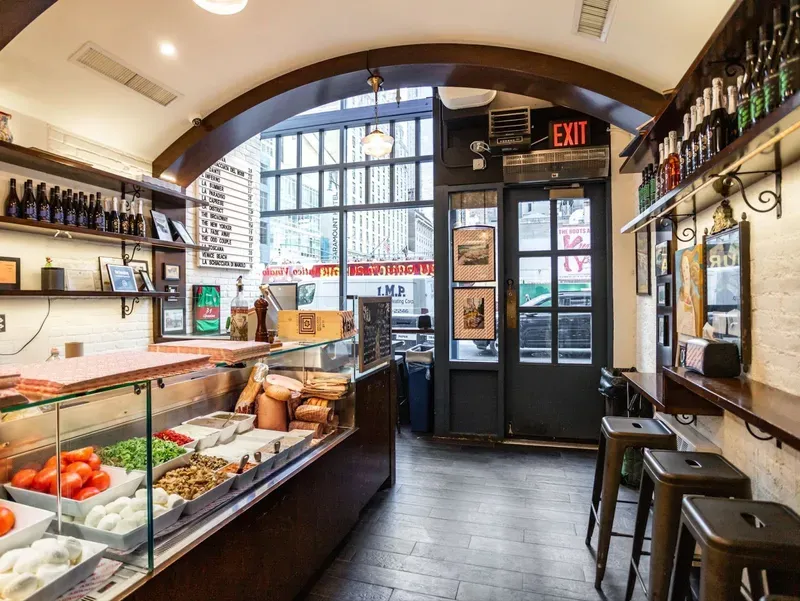 A restaurant with a glass display case filled with food and stools.