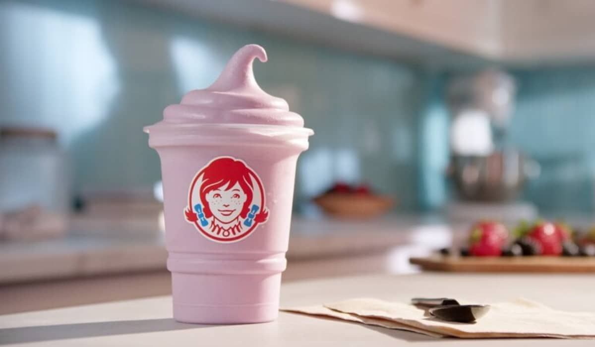 A pink cup of wendy 's ice cream is sitting on a table.