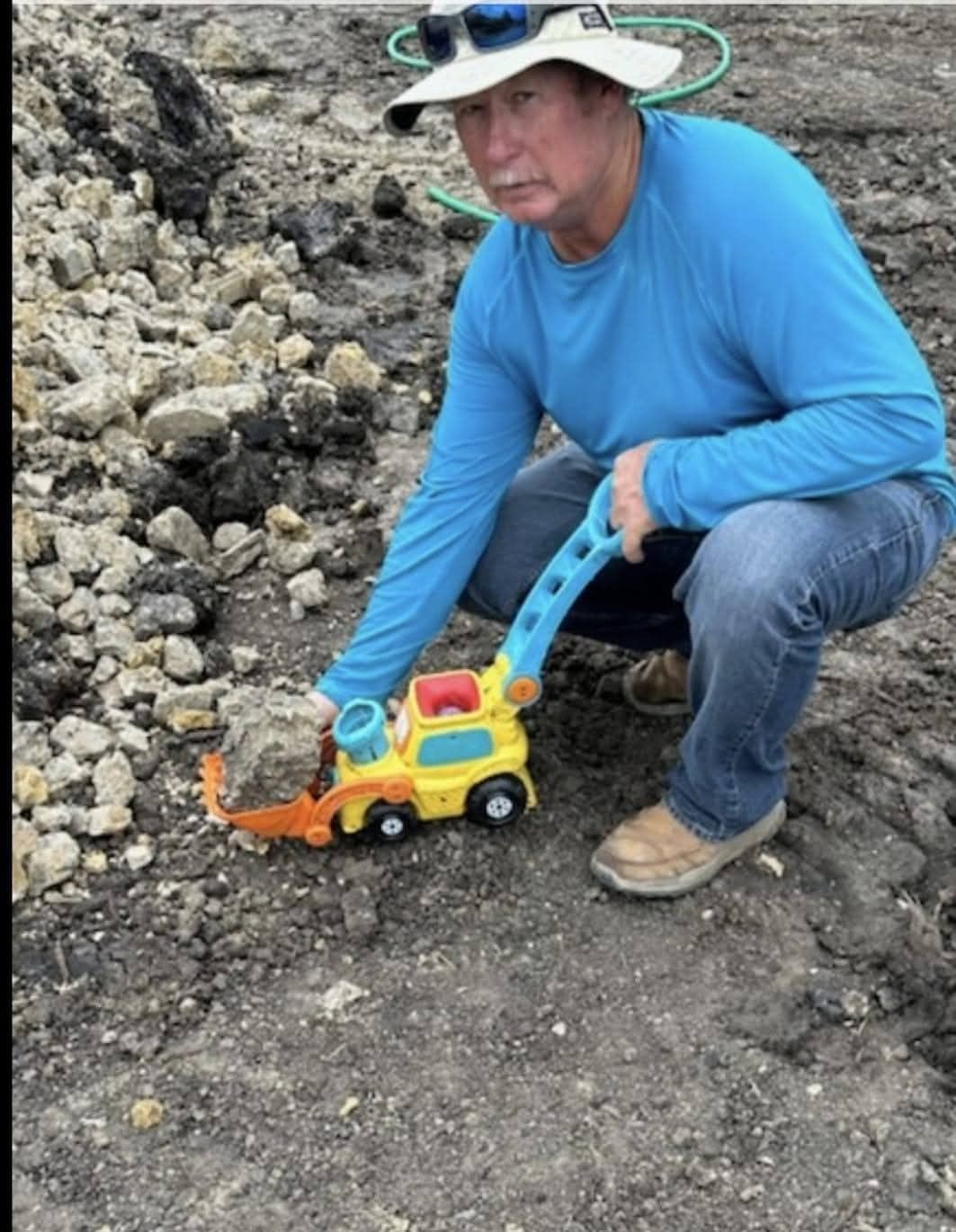 Woman in straw hat smiles, holding wine glass near a lake.