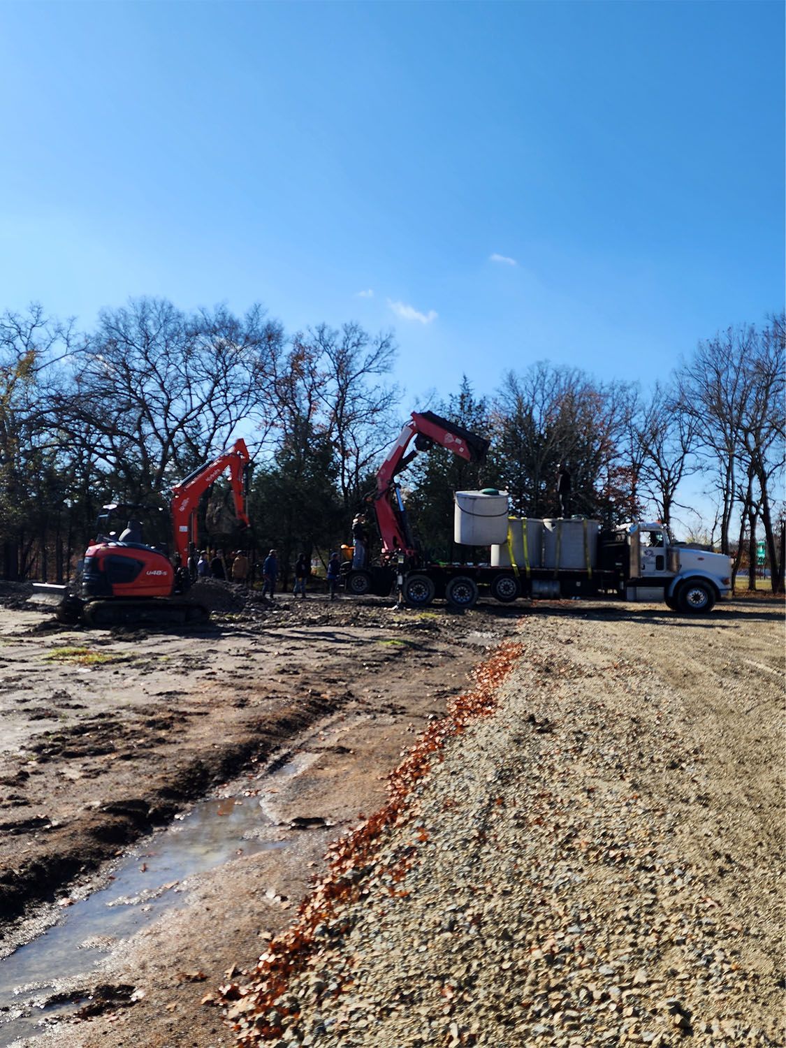 Woman in straw hat smiles, holding wine glass near a lake.