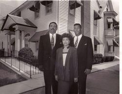 Three people in suits pose in front of a building with awnings.