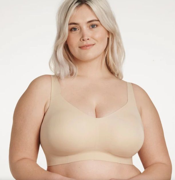 A woman is wearing a beige bra and smiling