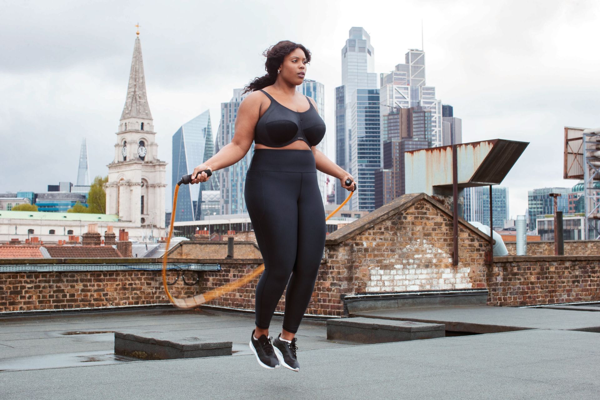 A woman is jumping a jump rope on a rooftop in front of a city skyline.