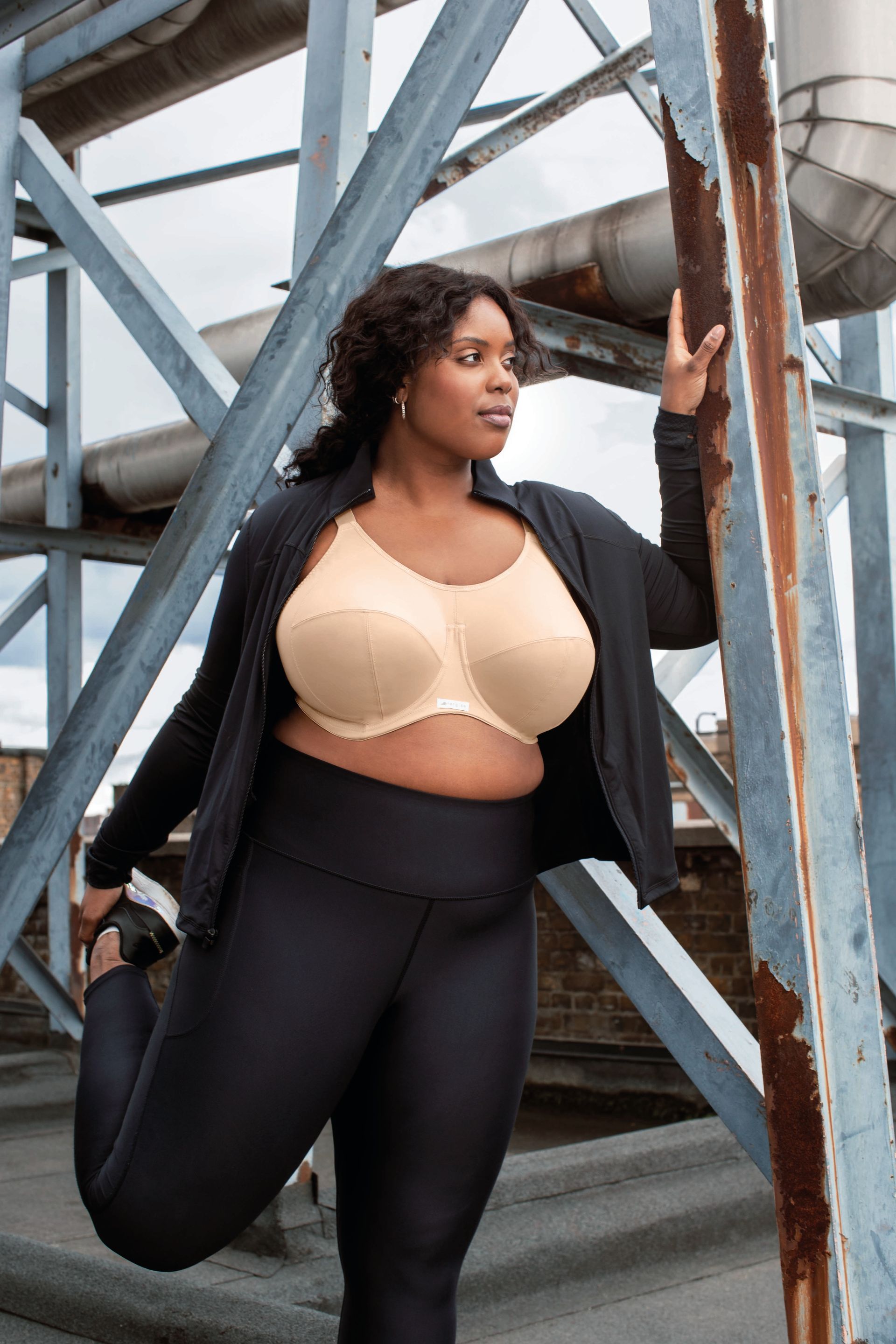 A plus size woman is stretching her leg in front of a metal structure.