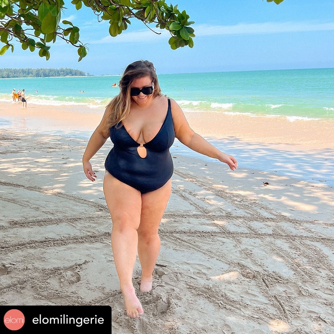 A woman in a black swimsuit is walking on the beach