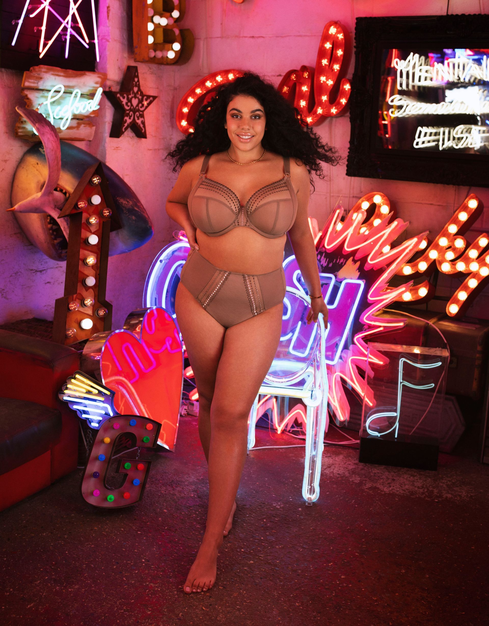 A woman in lingerie is standing in front of neon signs.