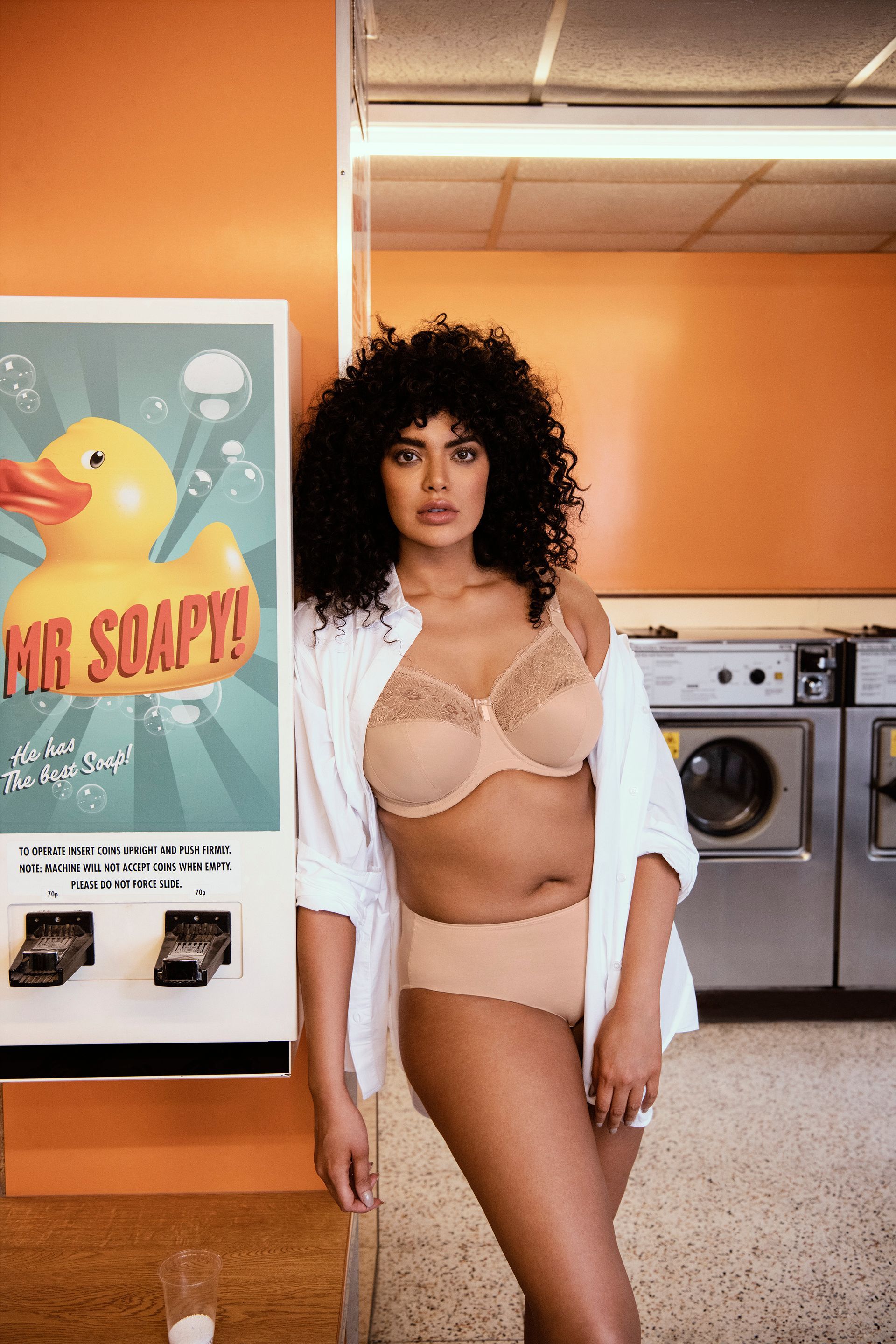 A woman in lingerie is standing in a laundromat next to a rubber duck.