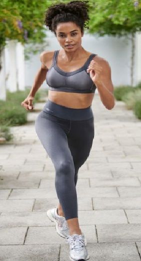 A woman in a sports bra and leggings is running on a sidewalk.