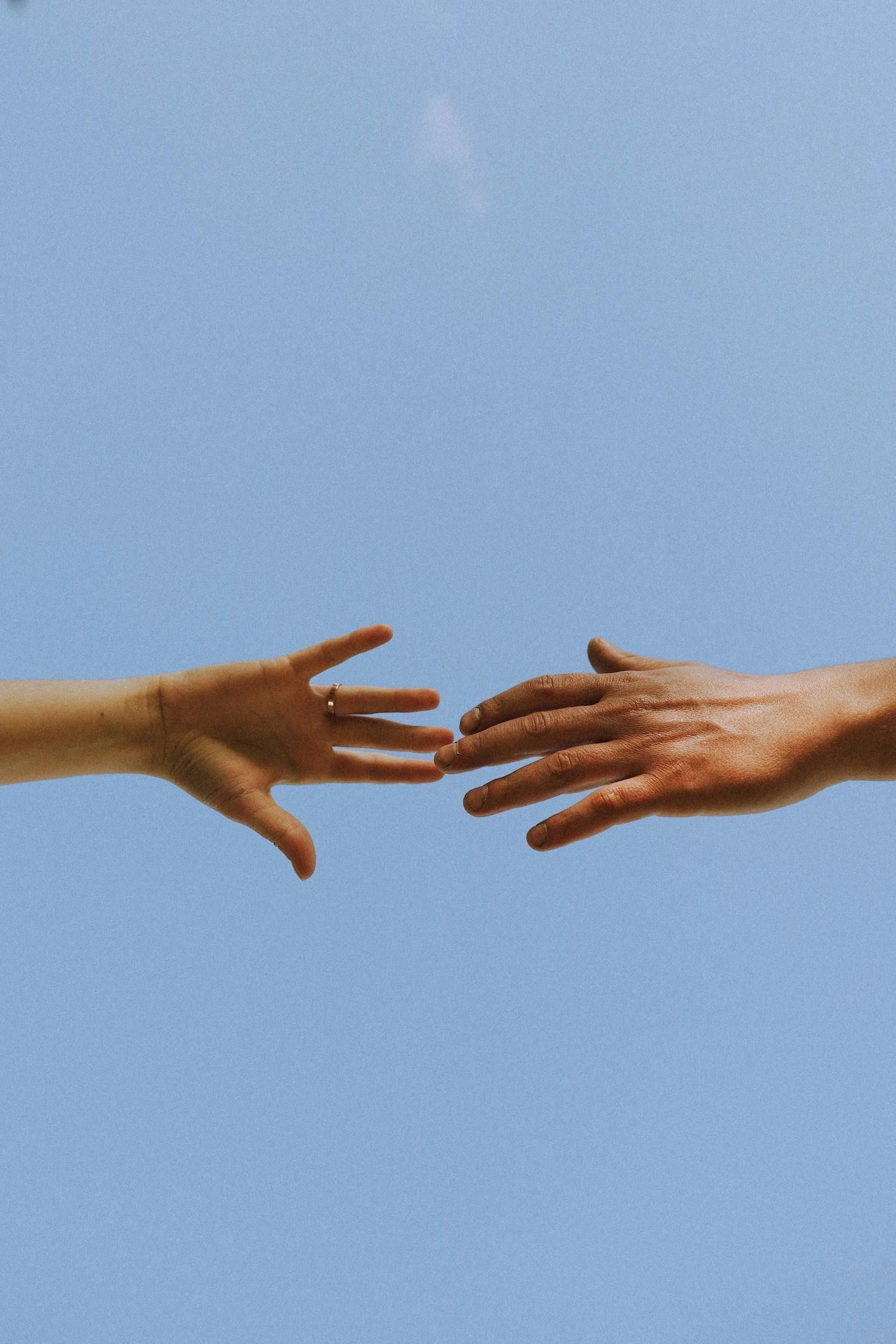 Two hands are reaching out towards each other against a blue sky.