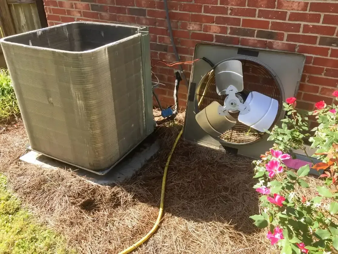 An air conditioner is sitting next to a fan on the side of a brick building.