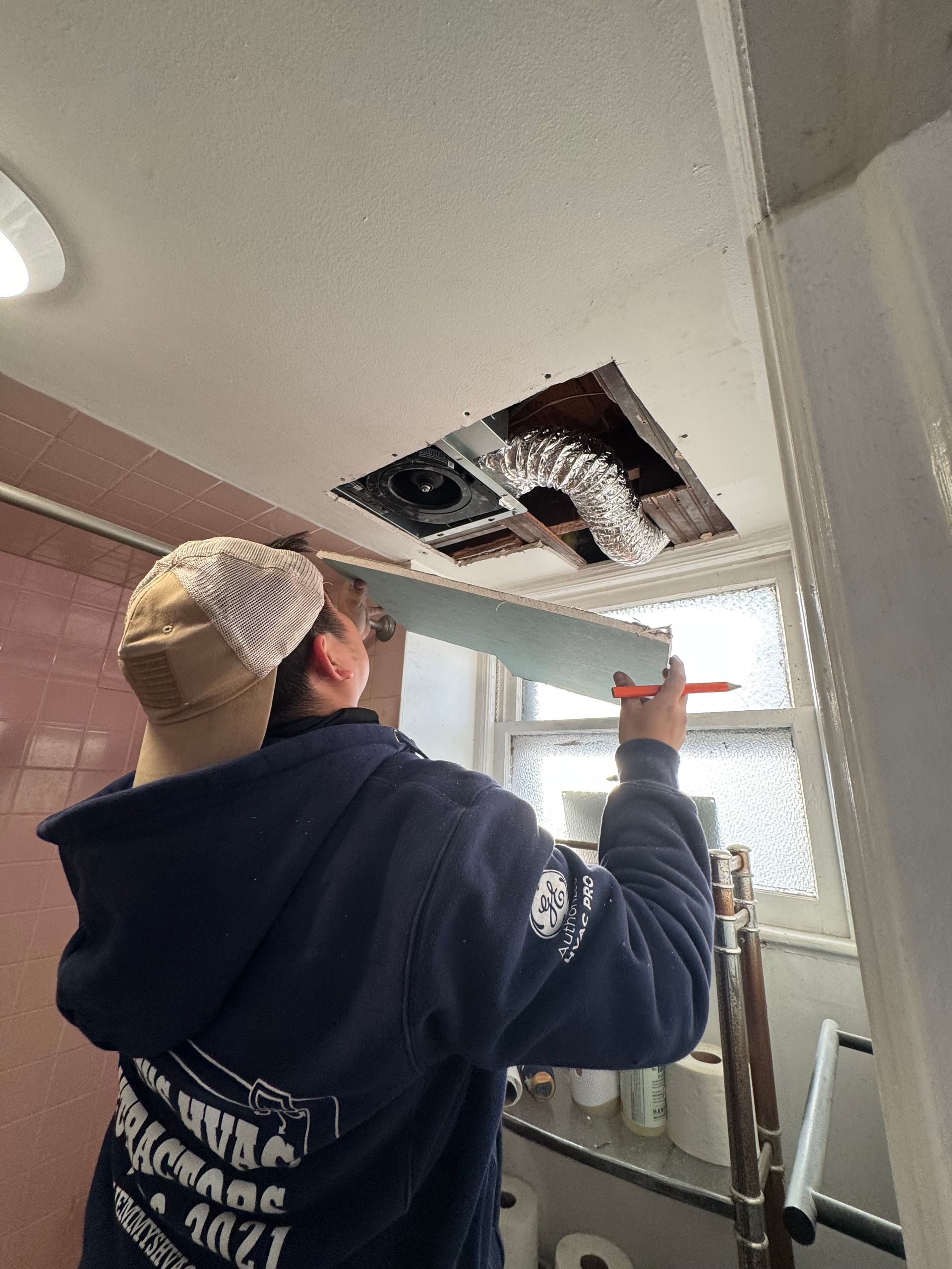 A man is working on the ceiling of a bathroom.