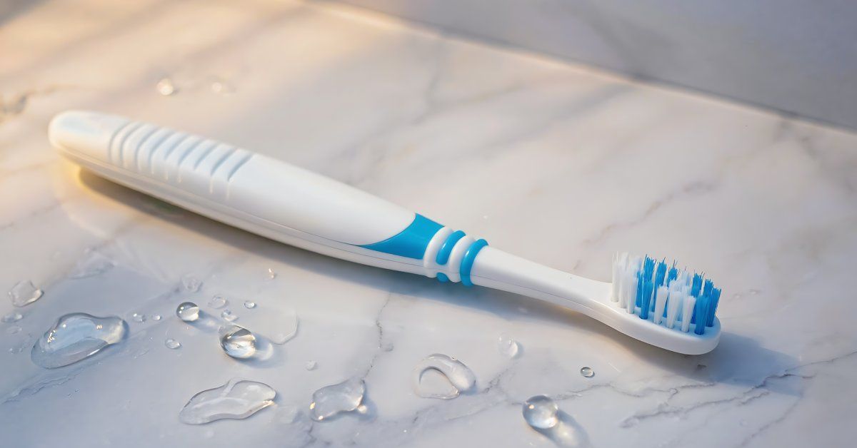 A blue and white plastic toothbrush resting on a marble bathroom countertop next to scattered water droplets.