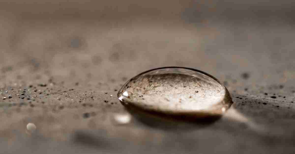 A close-up of a single water drop beaded on the surface of a sealed brown granite countertop.