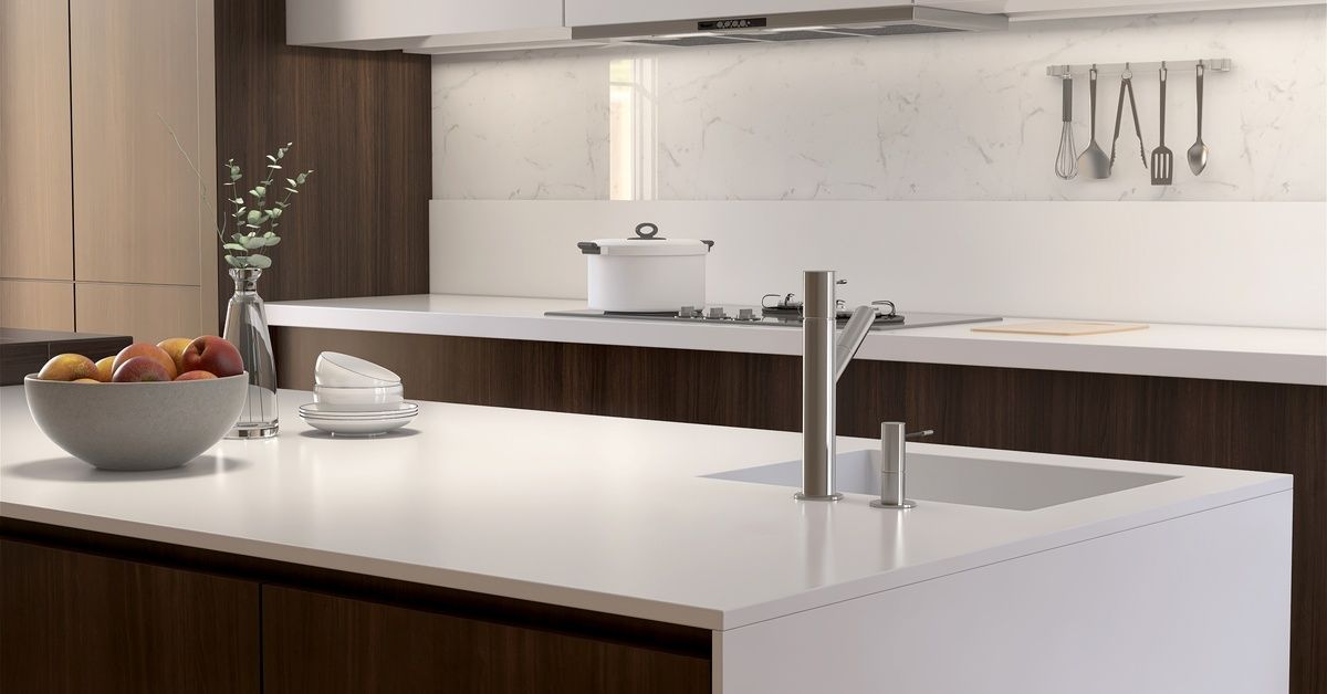 An island in a kitchen, the island has a sink installed into it. There is a bowl of apples on the island.