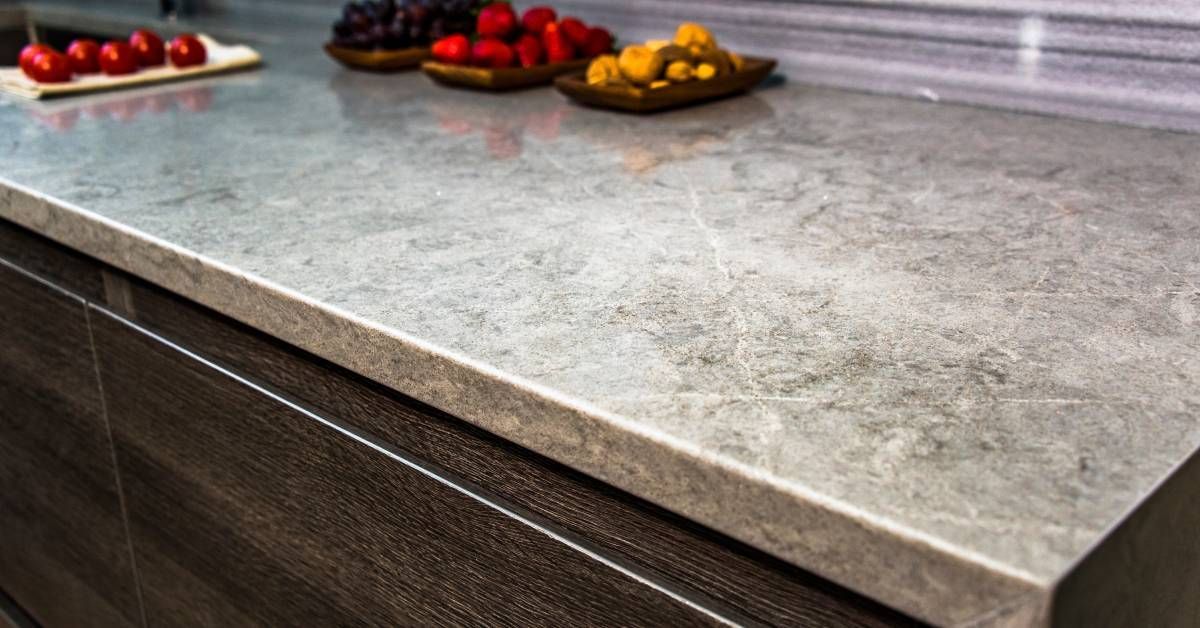 A granite countertop in a brightly lit kitchen. Four trays of assorted colorful fruits are on the co