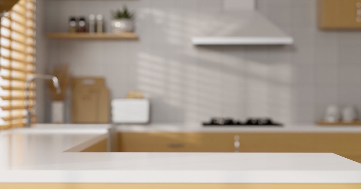 A large and dimly lit kitchen with a white countertop. The only light is the sunlight from a nearby 