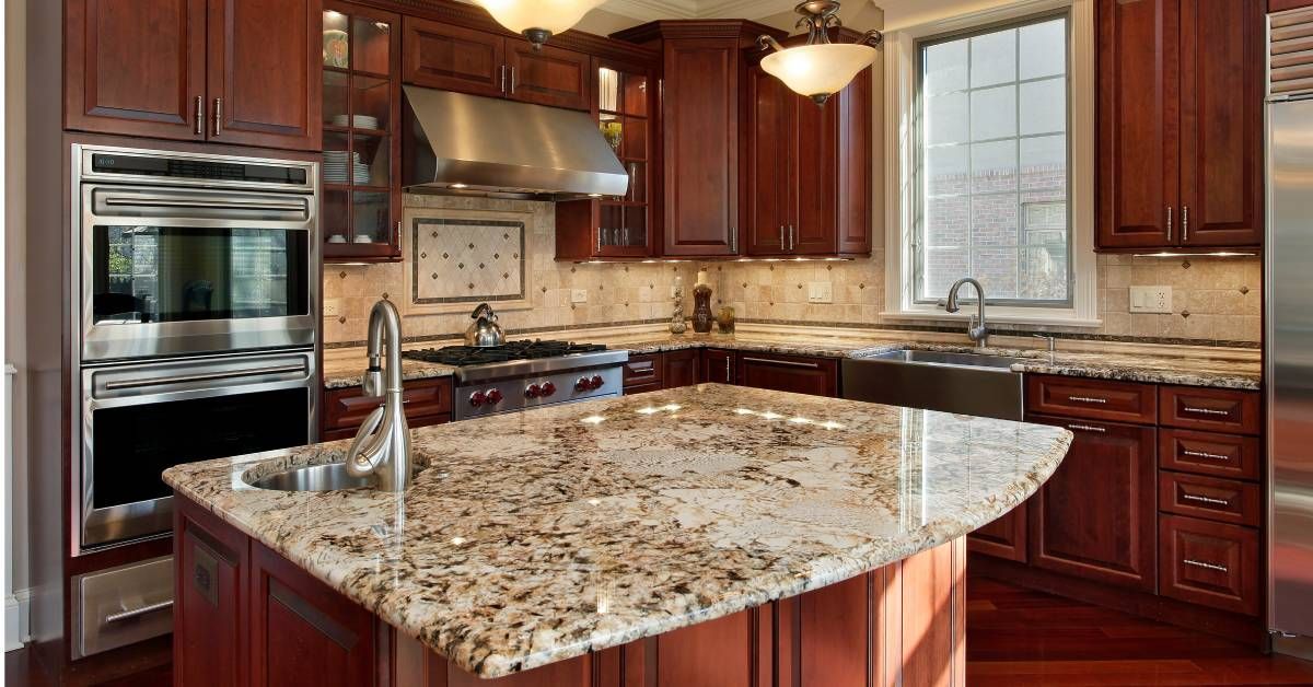 A kitchen with brown wooden floors and cabinets. An island with a granite countertop is in the middl