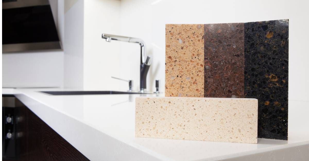 A clean kitchen with a large white countertop. Four granite samples in various earthy tones are sitting on the counter.