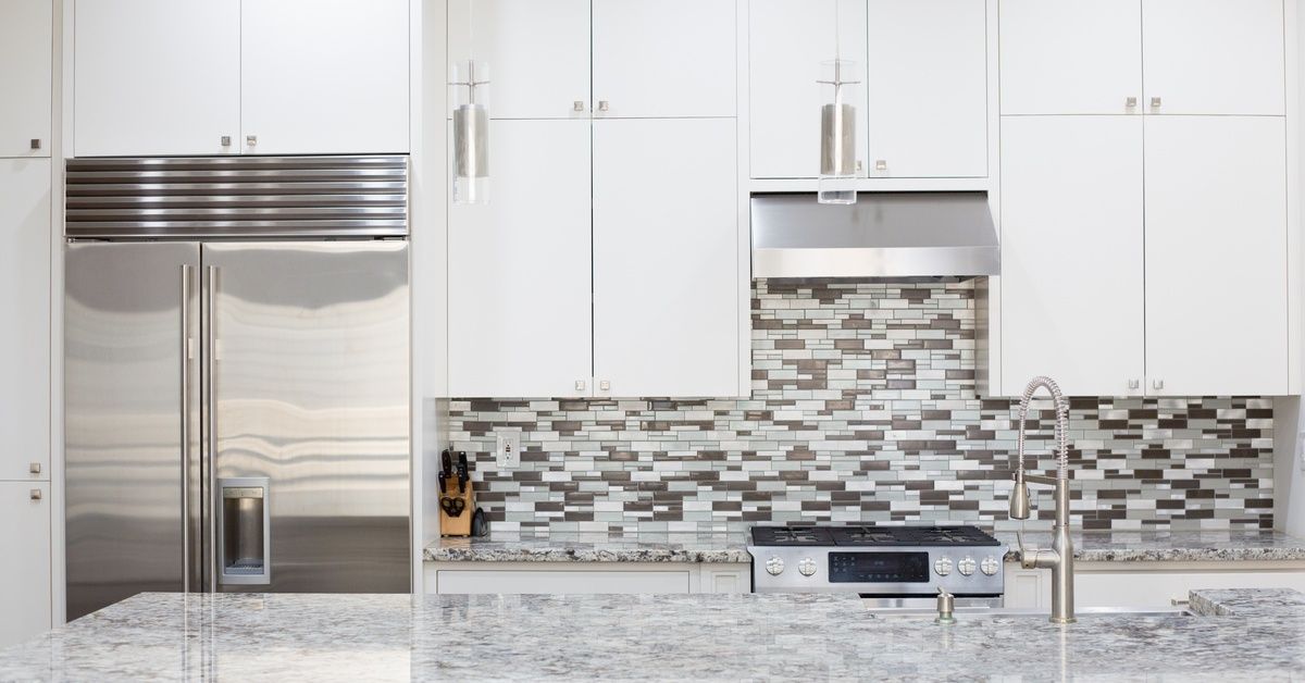 A large residential kitchen with a massive granite countertop and multi-colored tile backsplash.